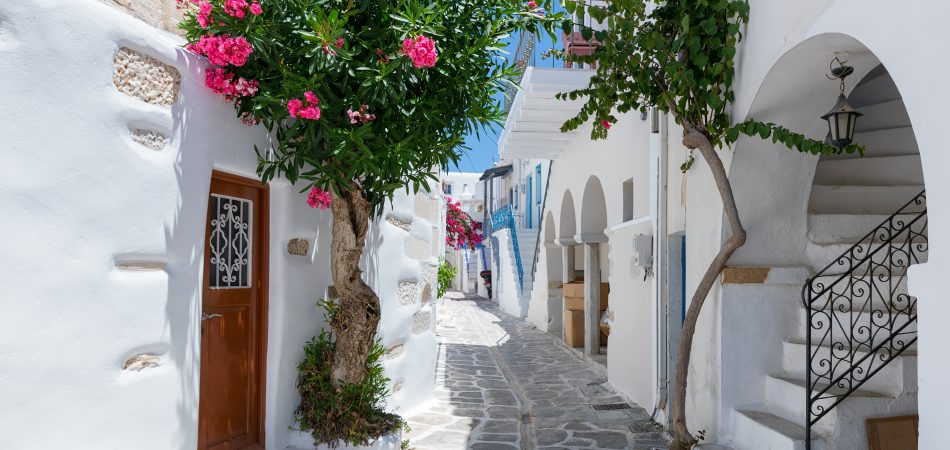 The-typical-cycladic-whitewashed-alleys-with-colorful-flowers-at-Parikia-on-the-island-of-Paros-Cyclades-Greece-during-summer-time-950x450